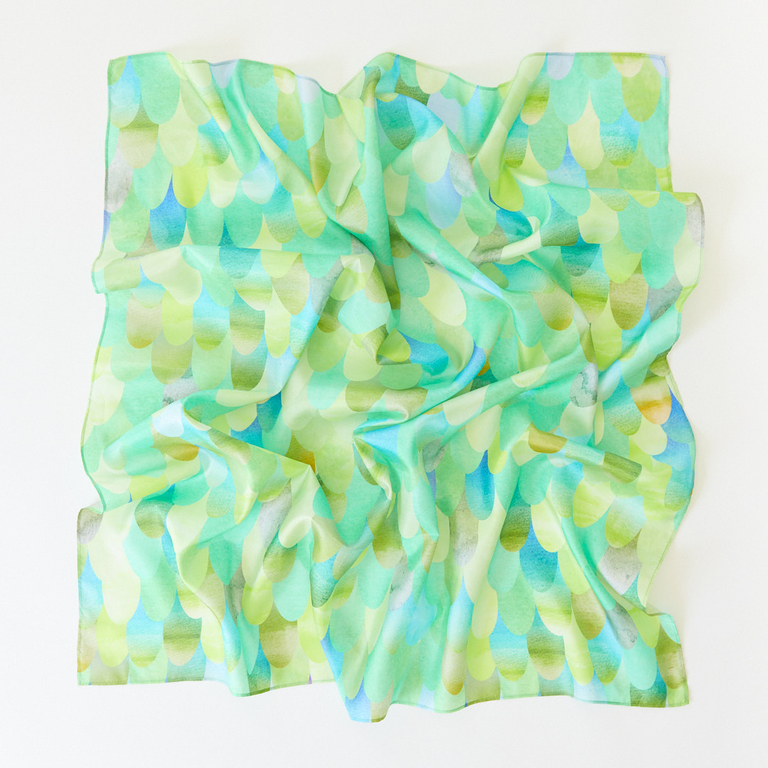 A crumpled square Playsilk, crafted from natural materials, features a green and blue scallop pattern on a white background—perfect for open-ended toys and imaginative play.